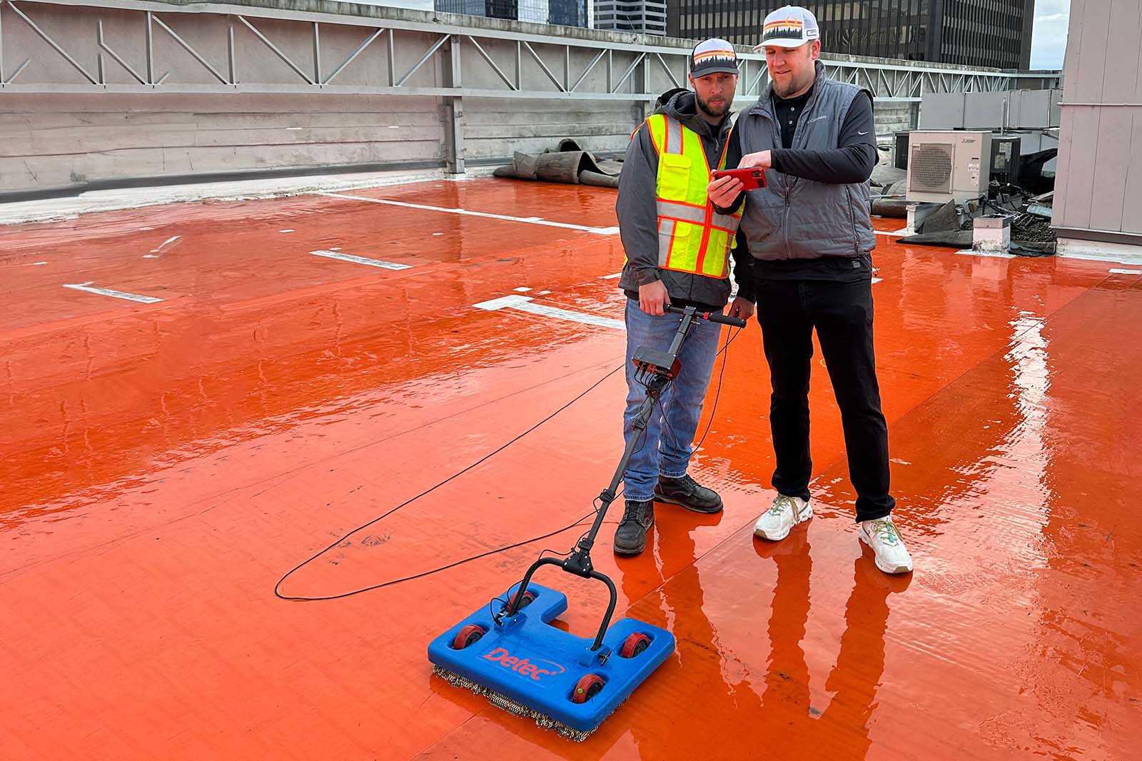 2 people checking the results of the electronic leak device on high rise roof